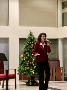 Woman singing near a decorated Christmas tree indoors.
