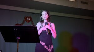 Woman singing on stage with a microphone and music stand.
