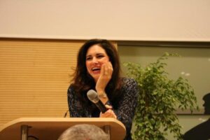 Woman laughing while speaking at a podium indoors.