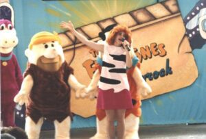 Characters in prehistoric costumes perform on stage at a themed event.