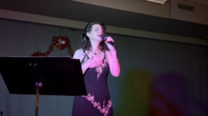Woman singing on stage with microphone and sheet music stand.