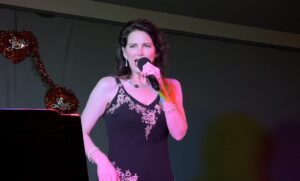 Woman singing on stage with a microphone in a black dress.