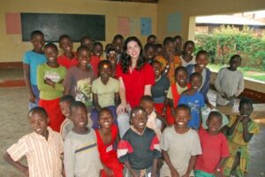 A woman in red surrounded by smiling children in a classroom.
