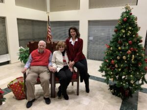 Three people posing indoors near a decorated Christmas tree.