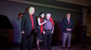 Four people in formal attire posing on stage with microphones.