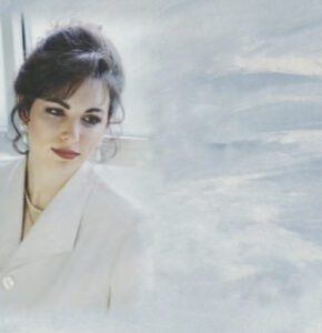 Portrait of a woman with dark hair in a white outfit against a soft, light background.